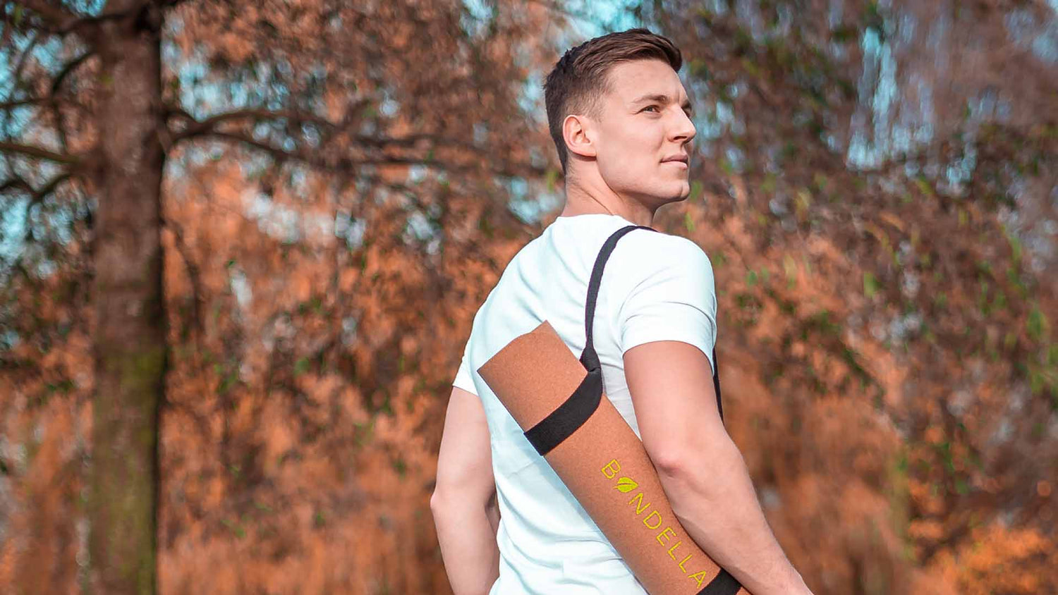 Junger Mann trägt die Bondella Ahimsa Kork Yogamatte mit dem Yoga Mat Strap um die Schulter